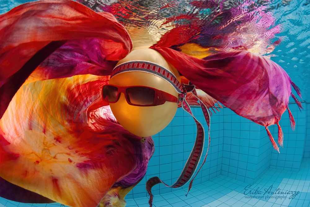 Goudkleurige ballon met zonnebril, bandanna en oranje-rode doek onder water in het zwembad