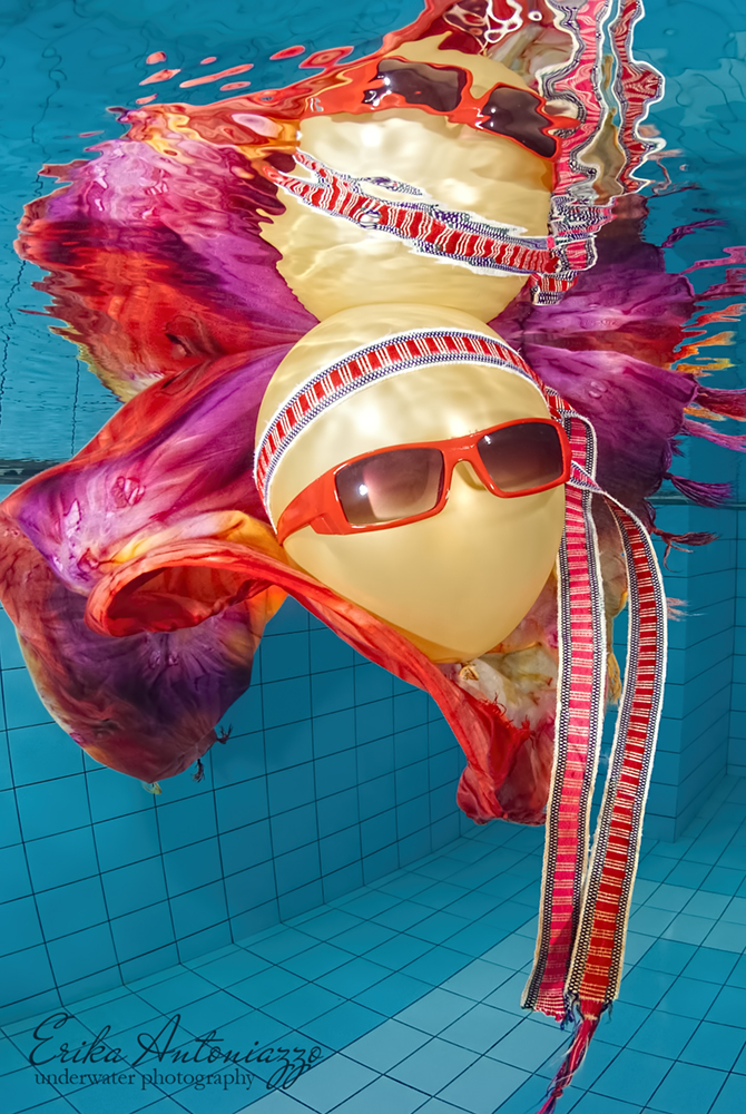 Goudkleurige ballon met zonnebril, bandanna en oranje-rode doek onder water in het zwembad