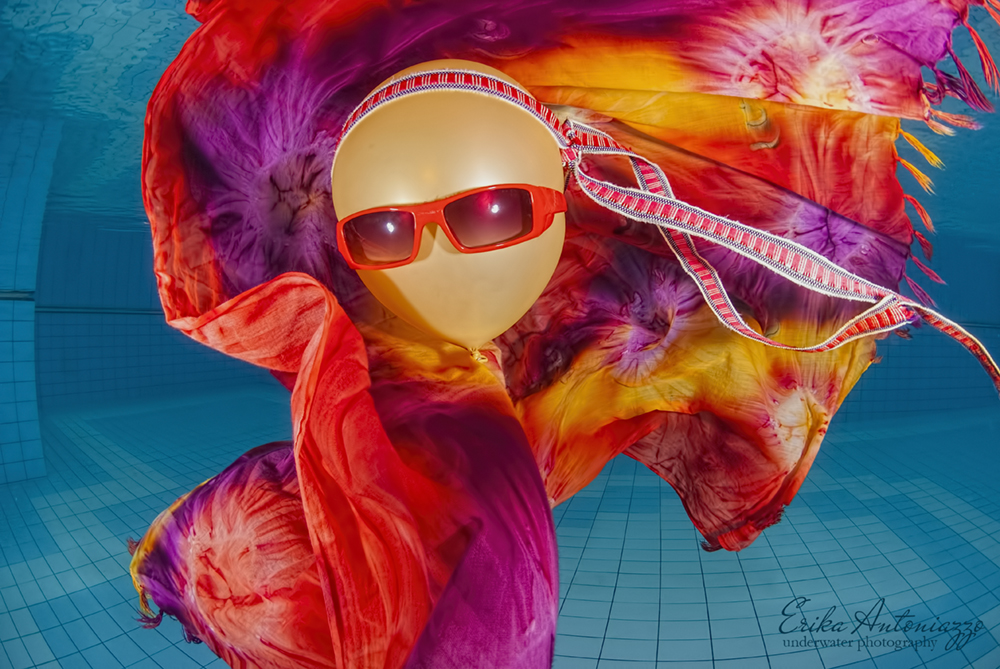 Goudkleurige ballon met zonnebril, bandanna en oranje-rode doek onder water in het zwembad